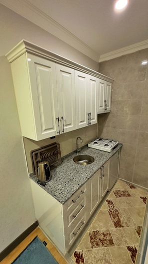 Cozinha compacta com armários brancos, uma pia de aço inoxidável e um fogão a gás.