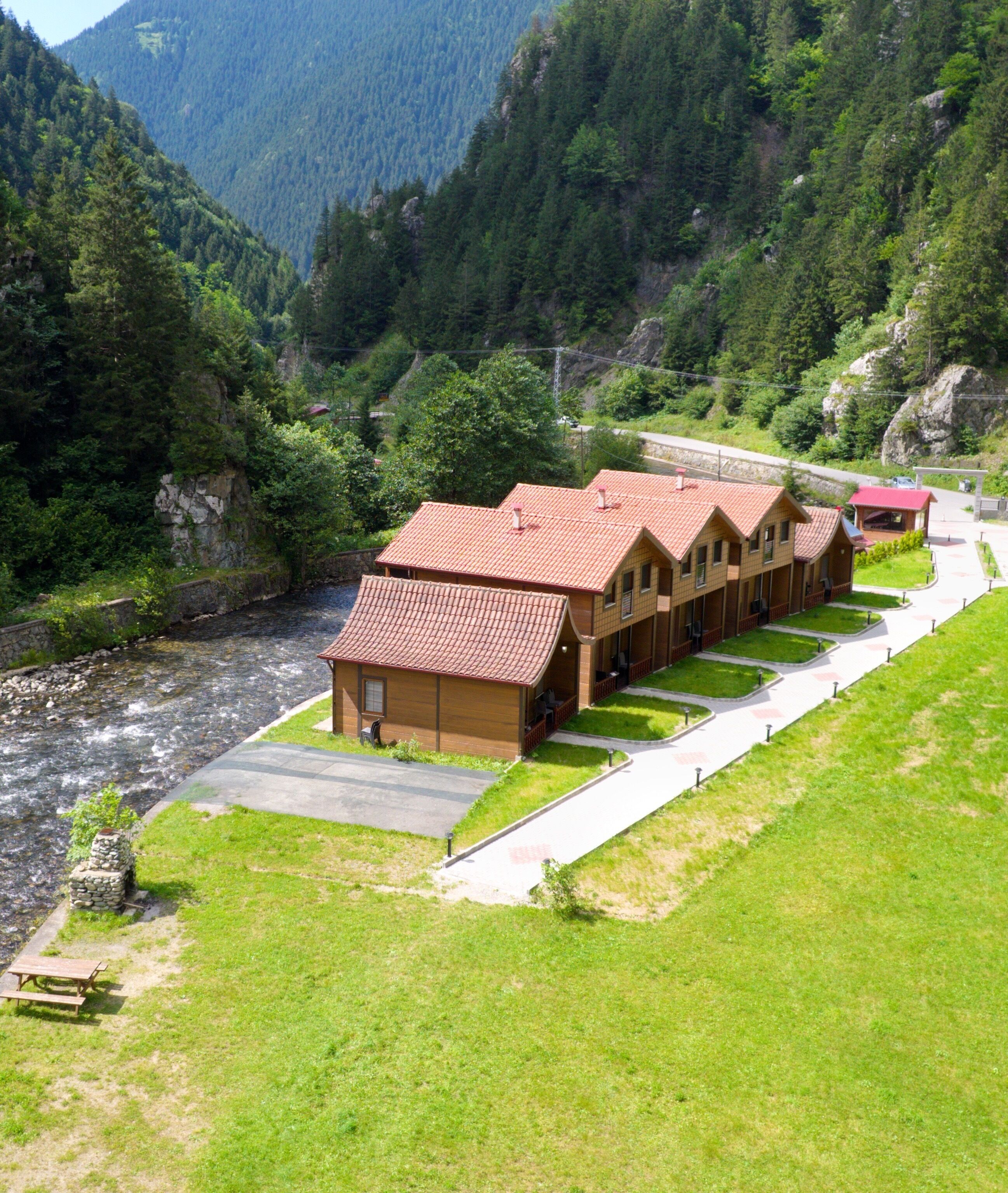 Una hilera de cabañas de madera con techos rojos, un sendero pavimentado y un río en primer plano.