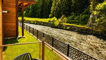 Un terrazzo in legno con tavolo e sedie affacciato su un fiume, con una collina boscosa sullo sfondo.