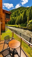 A wooden deck with a table and chairs overlooking a river, with a forested hillside in the background.