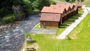 A row of wooden cabins with red roofs, a paved walkway, and a river in the foreground.