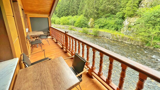 A wooden deck with tables and chairs overlooking a river and forest.