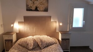 A bedroom with a bed, two bedside tables, a window, and a wall-mounted artwork of white roses.