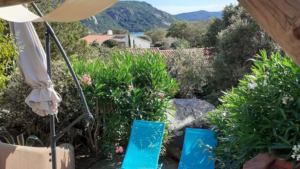A patio with two blue lounge chairs and a barbecue grill, overlooking a mountainous landscape.