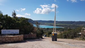 A sign for Bella Vista Vista Bella, a stone wall, a tall flagpole, and a view of a coastal landscape with mountains and a body of water.
