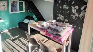 A room with a table stacked with towels, a chair, a staircase, and a wall with a floral mural.