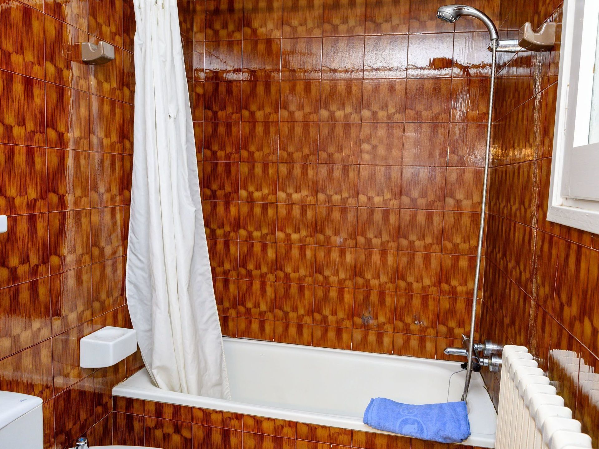 Un baño con pared de madera con azulejos, una bañera blanca, una cortina de ducha y un perchero para toallas.