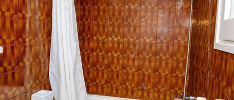 Un baño con pared de madera con azulejos, una bañera blanca, una cortina de ducha y un perchero para toallas.