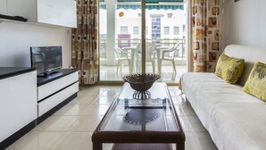 Un salon moderne avec un canapé, une table basse en verre, un téléviseur et un balcon équipé de chaises.
