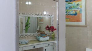 Un baño con tocador, espejo, lavamanos y un cuadro en la pared.