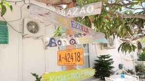 Un cartel de madera con varios indicadores direccionales, incluyendo uno para Aruba y otro para alquiler de kayaks y tablas de paddle surf.