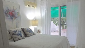 Quarto com cama, mesa de cabeceira, luminária, quadro e janela com cortinas.