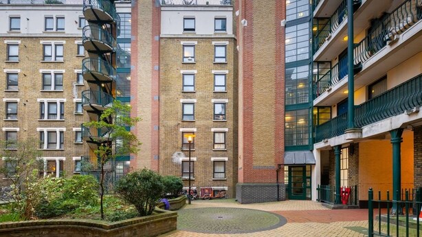 Un patio con un edificio de ladrillo, una valla metálica verde y una bicicleta estacionada cerca de la entrada.