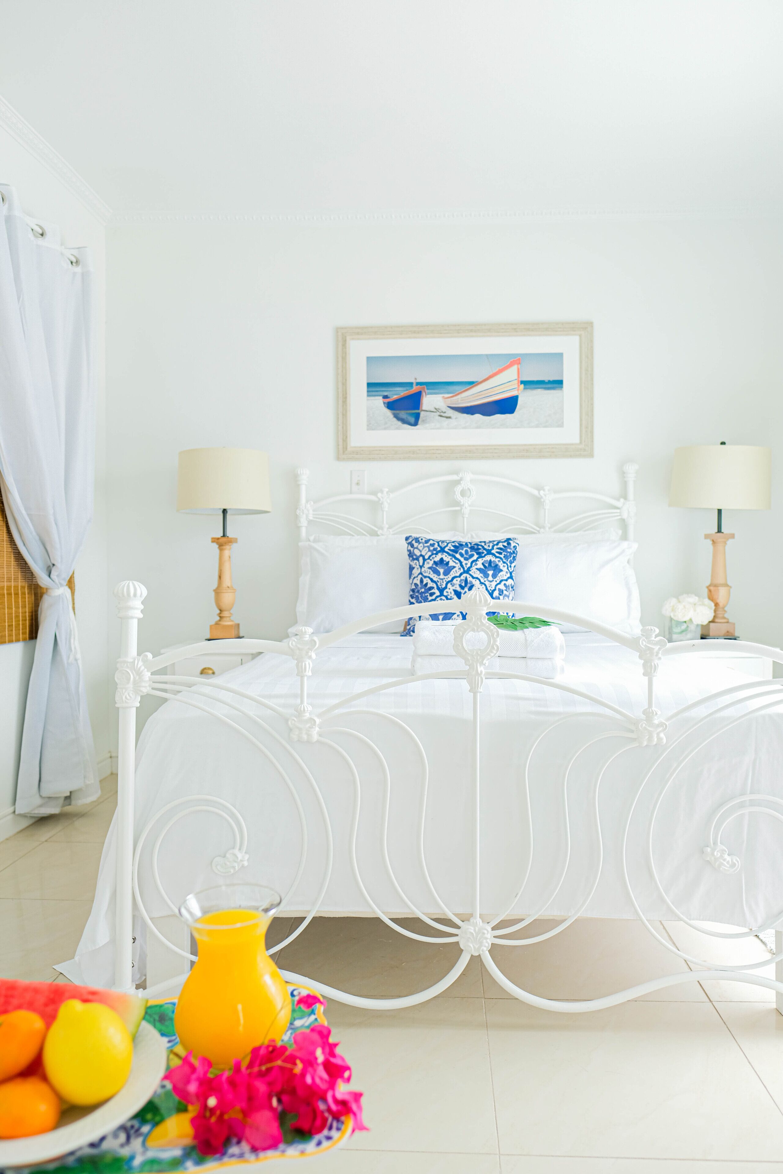 A white four-poster bed with a blue and white pillow, two bedside lamps, and a framed picture of a boat on the wall.