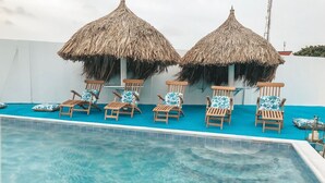A pool area with wooden lounge chairs and thatched umbrellas. - Ocean Front Property - Villa 2 Aruba (Savaneta)