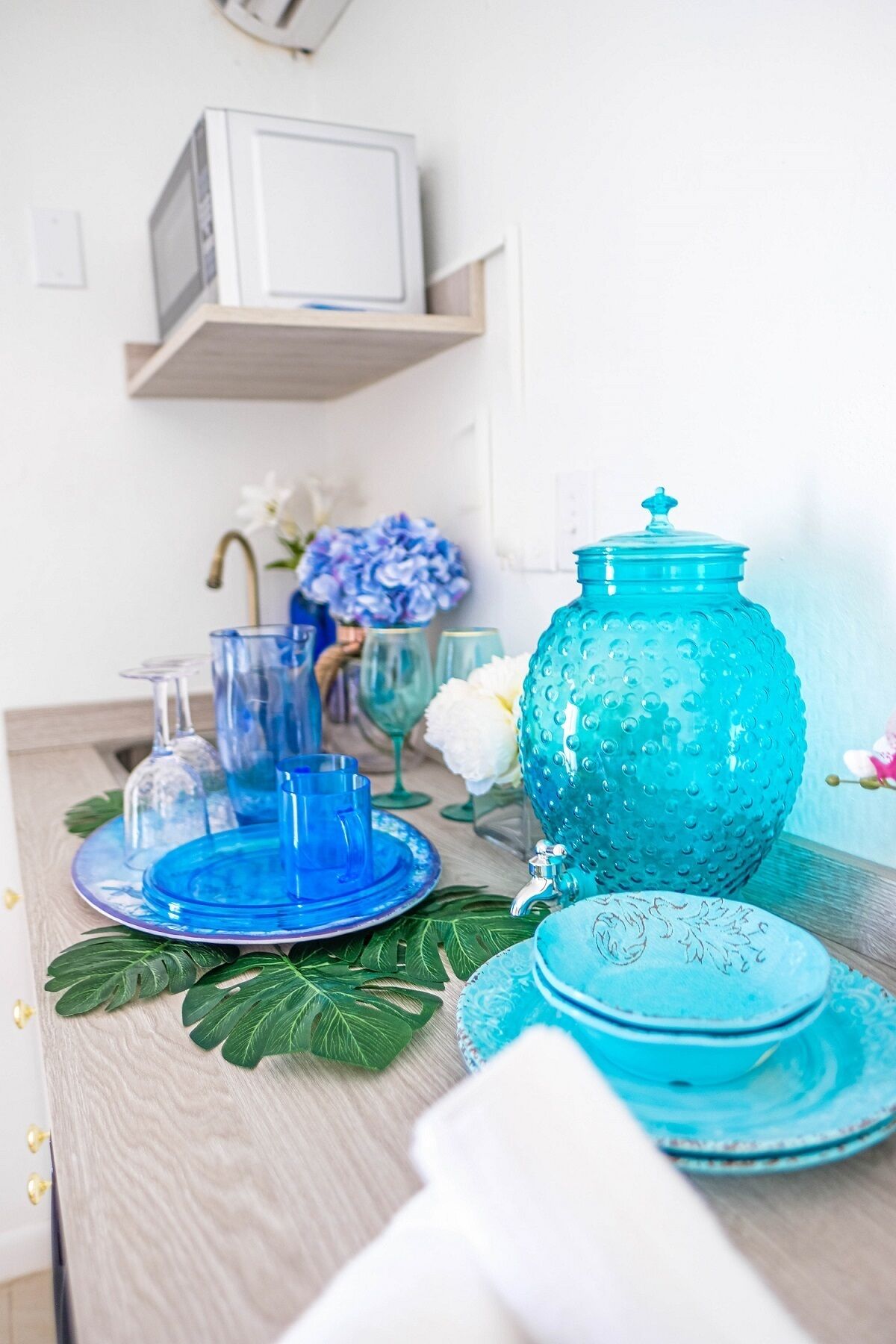 A table set with blue glassware and plates, a teal ceramic jug, and decorative leaves.