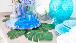 Una encimera de cocina con cristalería azul, un florero azul verdoso y hojas verdes.