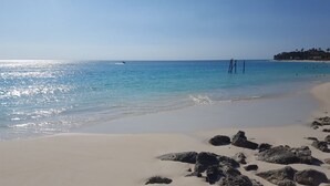 Una playa con agua azul cristalina, arena dorada y rocas.
