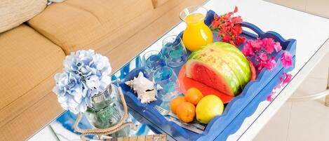 Un salón con sofá, una mesa de centro con revistas, una bandeja de frutas y objetos decorativos.