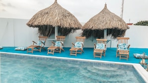 A swimming pool with wooden lounge chairs and thatched umbrellas.