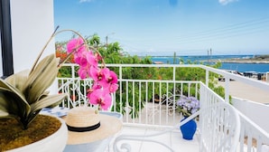 A balcony with a view of the sea, a potted plant, a straw hat, and a blue vase.