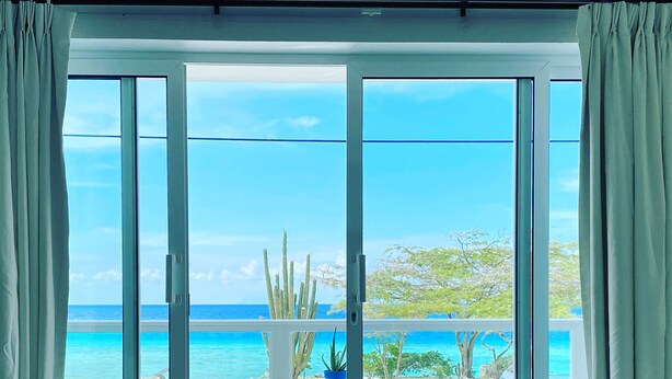 A room with a sliding glass door leading to a balcony with a view of the beach and ocean. - Beachfront Bella Horizonte 1 (Savaneta)