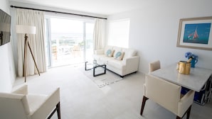A modern living room with a white sofa, a glass coffee table, and a dining table with a gold-colored pot. - Beachfront Bella Horizonte 1 (Savaneta)