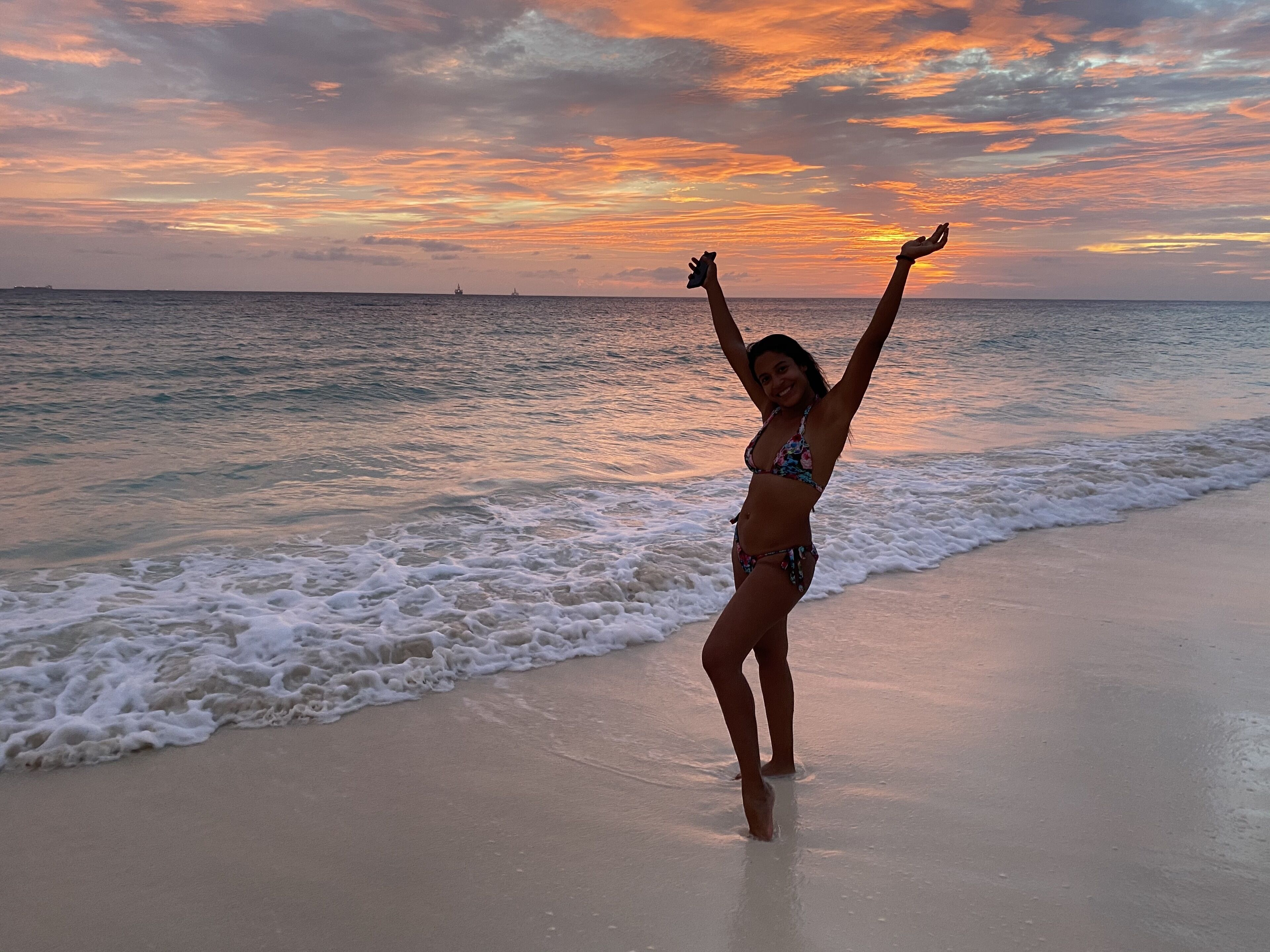 A beach scene with a person standing in the water, arms raised, and a sunset in the background.