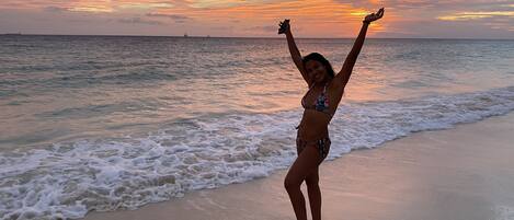 A beach scene with a person standing in the water, arms raised, and a sunset in the background.