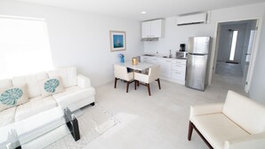 A modern, well-lit living room with a white sofa, a glass coffee table, and a dining area with a white table and chairs. A kitchen with white cabinets and stainless steel appliances is visible in the background. - Beachfront Bella Horizonte 3 (Savaneta)
