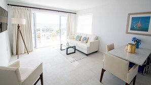 A modern living room with a white sofa, a glass coffee table, and a dining table with a gold-colored pot. - Beachfront Bella Horizonte 3 (Savaneta)