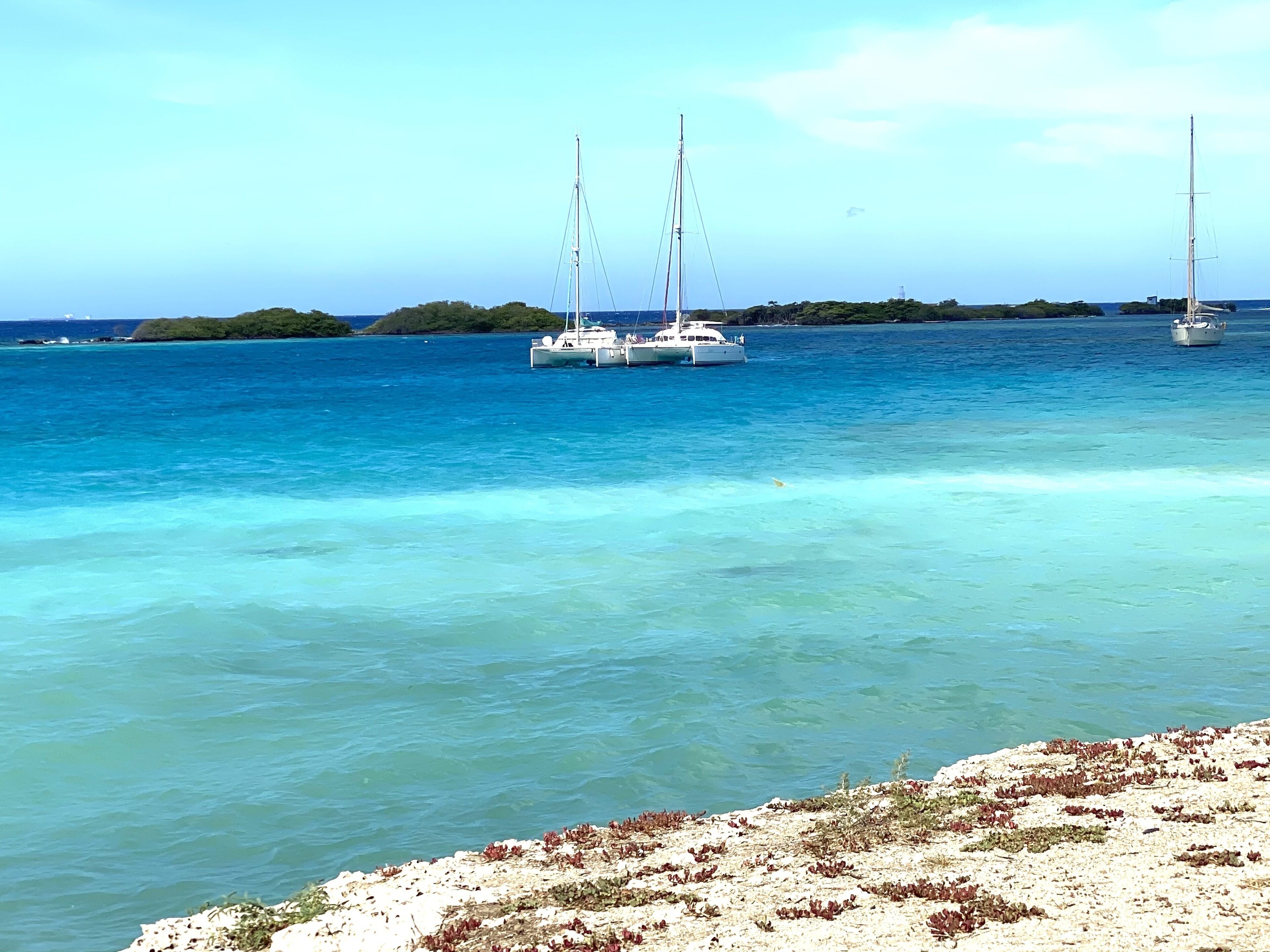 Una spiaggia con vista aperta, una barca a vela in acqua e un'isola all'orizzonte.