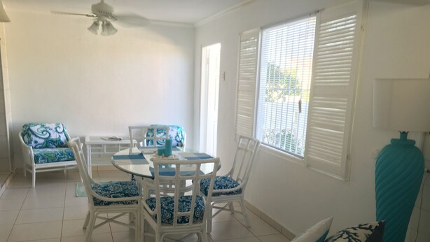 Uma sala de jantar com uma mesa redonda, cadeiras brancas e almofadas azuis com padrão.