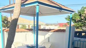 Uma área de pátio coberta com uma mesa, cadeiras, uma lixeira e um portão azul.