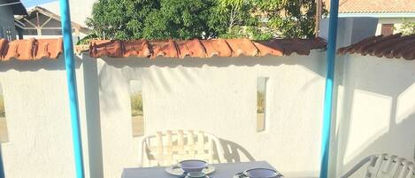 A covered patio area with a table set for two, featuring a white tablecloth and blue placemats.