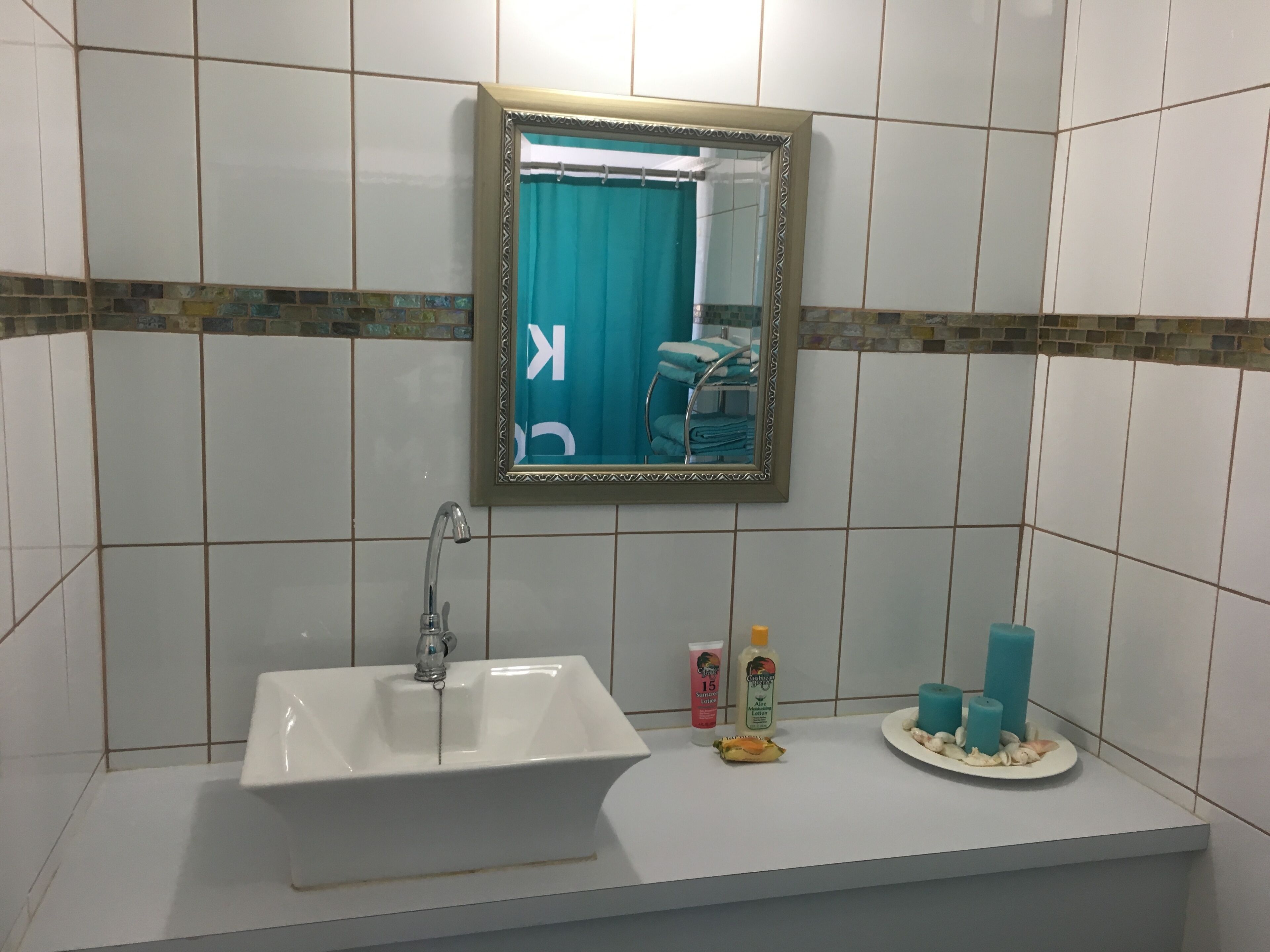 Un baño con lavamanos blanco, un espejo y artículos de aseo en la encimera.
