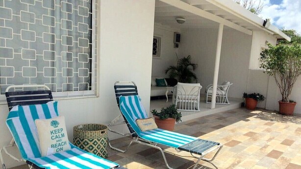 Un espace extérieur abrité comprenant deux fauteuils de jardin et une table, une plante en pot et une fenêtre décorée.