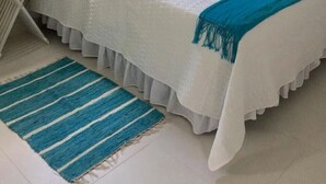 Une chambre à coucher avec un lit, une table de chevet, une lampe, une fenêtre et un tapis à rayures bleues.