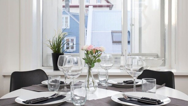 A dining table set with plates, cutlery, and glasses, with a vase of flowers and a potted plant on the windowsill. - Stunning 2BR apt with balcony view in Reykjavik (Reykjavík)