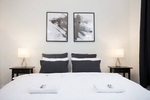 Ett hotellrum med en stor säng, två sängbord, två lampor och två abstrakta tavlor på väggen.