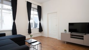 A modern living room with a sofa, a TV on a stand, a small table with a vase, and a window with curtains. - Stunning 2BR apt with balcony view in Reykjavik (Reykjavík)