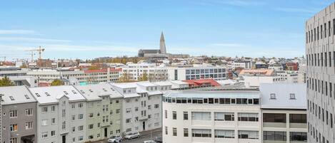 Eine Stadtansicht mit modernen Gebäuden, einem markanten Turm und einer Straße mit parkenden Autos.