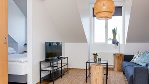 A modern, compact living space with a TV on a black stand, a wooden coffee table, a sofa, and a large window with a view of the outside. - Tyr 1BR apartment (Reykjavík)