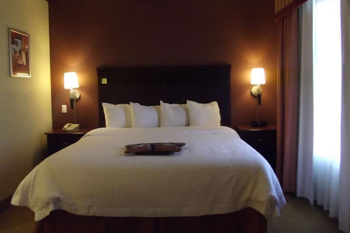 Habitació d'hotel amb un llit gran, dues taules de nit, un capçal de llit i dues làmpades de paret.