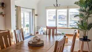 Un coin repas avec une table en bois, des chaises et une vue sur une étendue d’eau grâce à de grandes fenêtres.