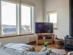 Una sala de estar acogedora con un ventanal grande, un televisor sobre un soporte de madera, un sofá, una chimenea y vistas al exterior.