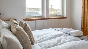 Une chambre à coucher avec un lit, deux fenêtres, une tête de lit en bois et un radiateur.