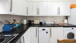 A modern kitchen with white cabinets, a dishwasher, a washing machine, and a coffee maker. - Ealing garden flat by Walpole Park (London)