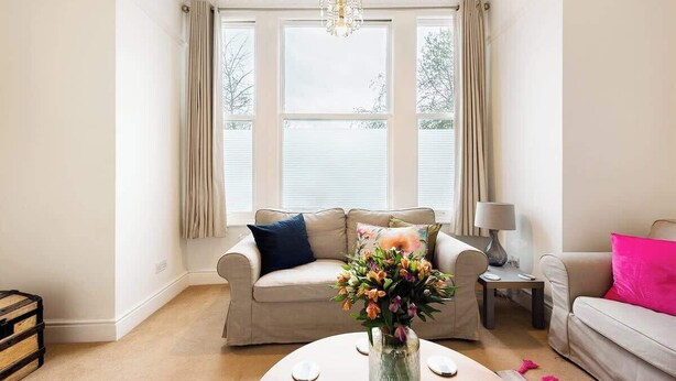 A living room with a beige sofa, a coffee table with a vase of flowers, and a chandelier. - Ealing garden flat by Walpole Park (London)