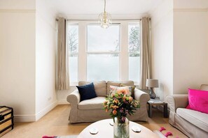 A living room with a beige sofa, a coffee table with a vase of flowers, and a chandelier.